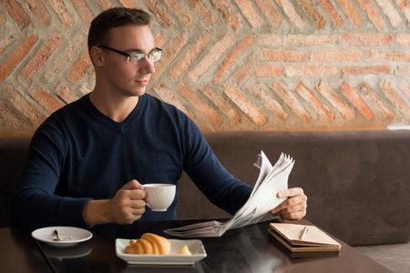 Smiling handsome businessman spending morning with newspaper and cup of coffee