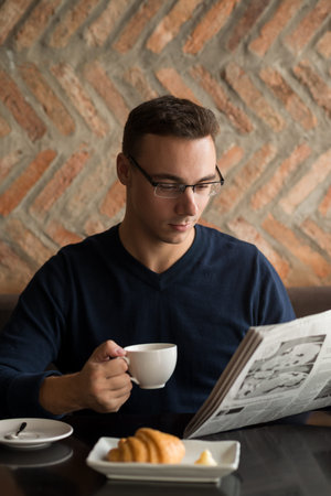 Young man enjoying cup of coffee and morning newspaper