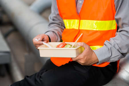 Cropped image of engineer in bright orange vest eating salad for lunchの写真素材