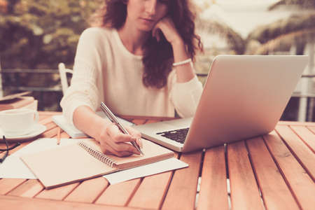 Woman working on computer and writing down her thoughtsの写真素材