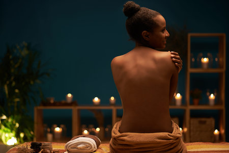 Rear view of gorgeous naked woman sitting on the massage bed after having spa procedureの写真素材