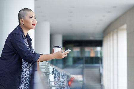 Beautiful bald woman drinking coffee and contemplating at the business centerの写真素材