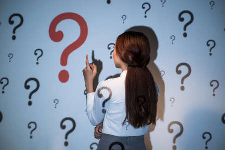Rear view of young business lady looking at the wall with many question marksの写真素材