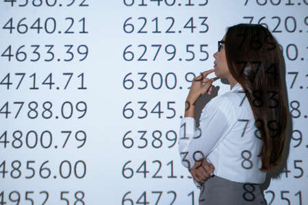 Pensive financial manager looking at the wall with different numbers: economics and financial managementの写真素材