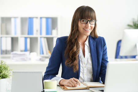 Business lady in glasses sitting at her workplace in the officeの写真素材