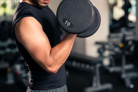Cropped image of sportsman with heavy dumbbell working on bicepsの写真素材