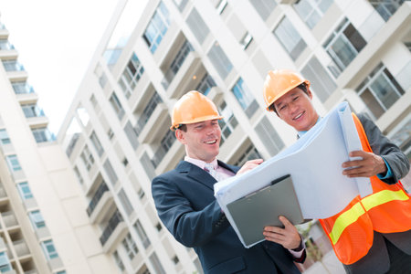 Multi-ethnic colleagues in hard hats discussing blueprint of the house