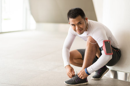 Smiling sportsman tying shoelaces before jogging