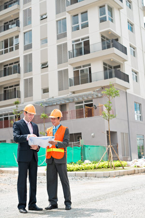 Contractor and investor standing in front of the building and discussing construction plan