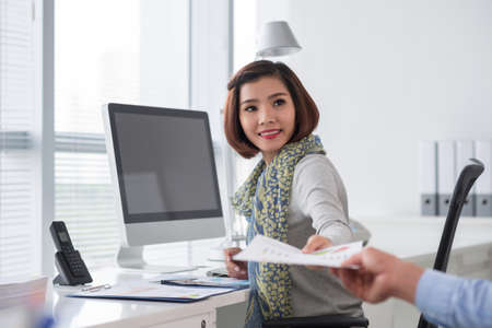 Pretty smiling business lady giving document to her coworkerの写真素材