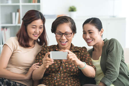 Senior woman, her daughter and granddaughter watching funny video on the smartphoneの写真素材