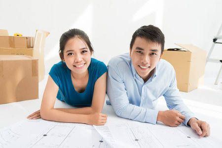 Relocation and renovation: couple lying on the floor with blueprints of the house