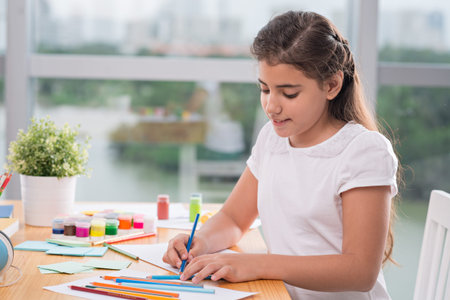 Smiling schoolgirl drawing with pencils at homeの写真素材