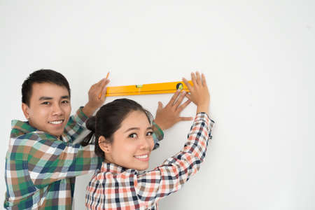 Vietnamese young couple using level to do marks on the wallの写真素材