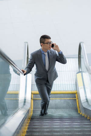 Businessman going up the escalator and calling on the phoneの写真素材