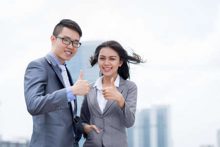 Asian business colleagues standing outdoors and showing thumbs upの写真素材