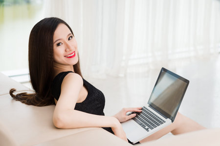 Beautiful elegant woman sitting on the sofa and using laptopの写真素材