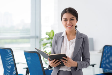 Young Asian female entrepreneur with notepad standing in the office