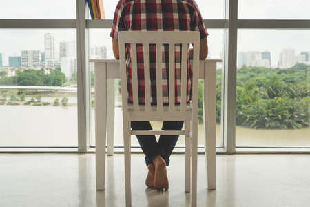 Cropped image of man working at the table in front of large window, view from the backの写真素材