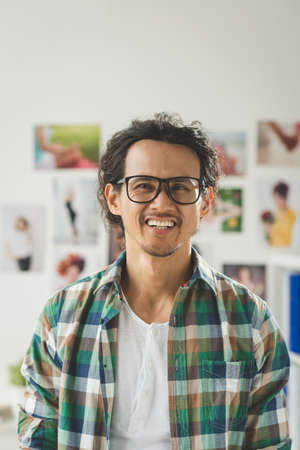 Cheerful creative young man in check shirt and glasses looking at the cameraの写真素材