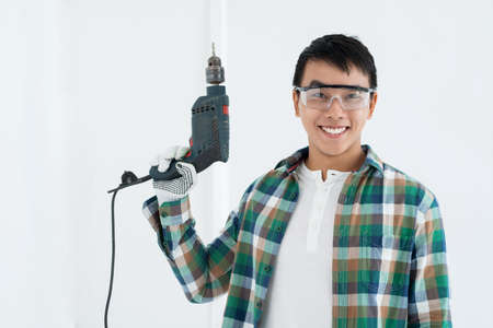 Cheerful Asian handy man in goggles holding a drillの写真素材