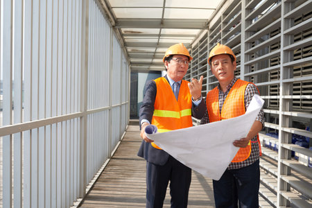 Asian businessman explaining blueprint to contractor at site