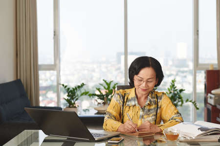 Senior Asian business woman sitting at table and taking notesの写真素材