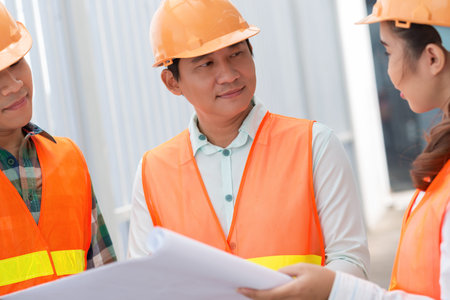 Portrait of middle-aged Vietnamese engineer talking to his coworkers