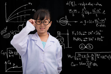 Vietnamese girl in glasses and labcoat standing at the blackboard with formulasの写真素材