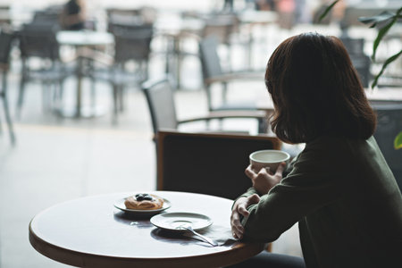 Pensive woman having breakfast in the café, view from the backの写真素材