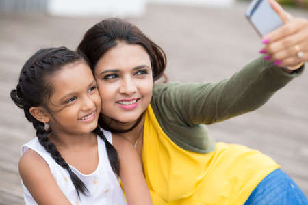Smiling Indian mother and daughter hugging and taking selfieの写真素材