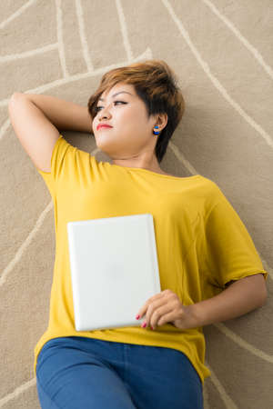 Contemplating young woman lying on the floor with a tablet computer in her handの写真素材