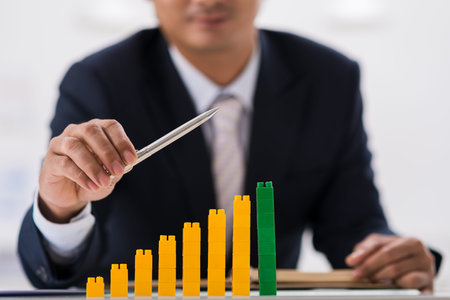 Financial manager using pen and chart made of colored plastic bricks to indicate business...