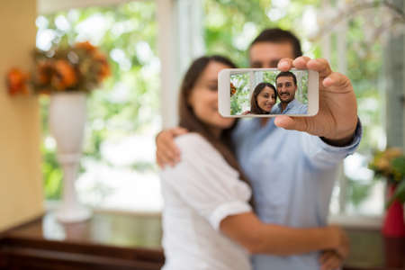 Hugging couple taking selfie, focus on the smartphone screenの写真素材