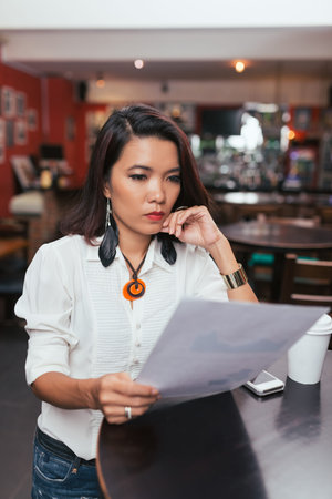 Vietnamese bar owner standing at the table and reading financial reportの写真素材