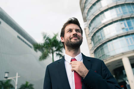 Stylish businessman adjusting necktie while standing outdoorsの写真素材