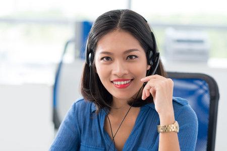 Female operator of call-center in headphones holding microphone