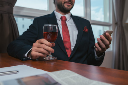 Cropped image of business person drinking wine and reading message on his phoneの写真素材