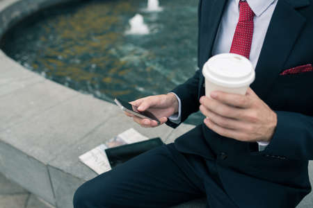 Businessman drinking coffee and texting outdoors, selective focusの写真素材