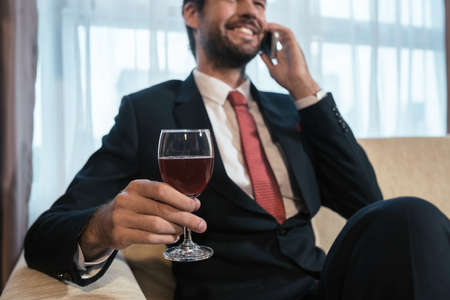 Business person drinking wine and talking on the phone, focus on wineglassの写真素材