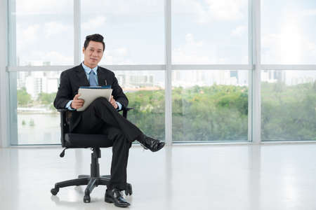 Smiling Vietnamese businessman with folders sitting in a chairの写真素材