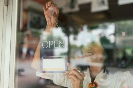 Smiling woman hanging open sign on the glass doorの写真素材