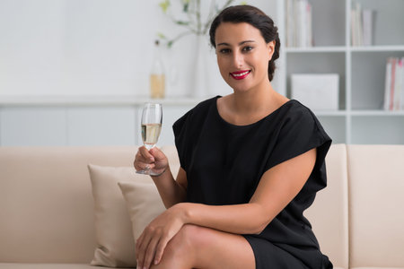 Gorgeous woman holding a glass of white wine and looking at the cameraの写真素材