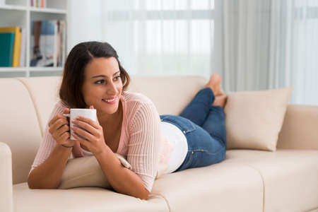 Beautiful young woman lying on the sofa and drinking coffeeの写真素材