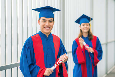 Cheerful graduates posing outdoors in gowns and hatsの写真素材