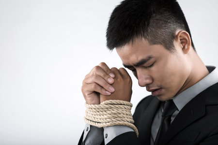 Asian businessman with chained hands lowering headの写真素材