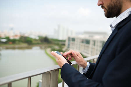Businessman using his smartphone outdoors on balconyの写真素材
