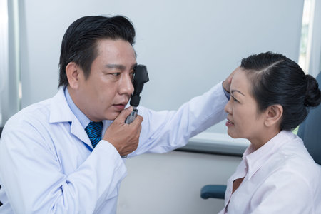 Optometrist using ophthalmoscope while examining female patient