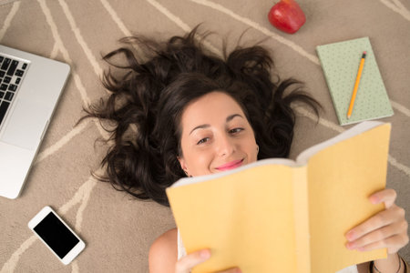 Mid-adult woman lying on floor and readingの写真素材