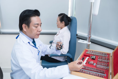 Mature Vietnamese optometrist choosing lens for trial frames